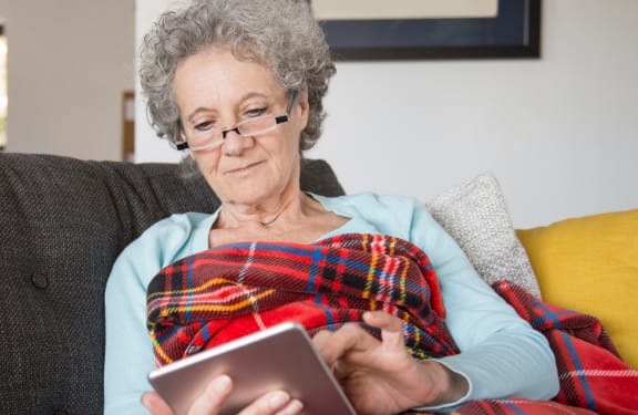 Woman on the couch wrapped in a blanket browsing her tablet